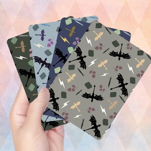 Op de afbeelding: Een hand die een stapel kaarten met patronen vasthoudt. Elke kaart heeft een ander kleurenschema met herhaalde illustraties van draken, bliksemschichten en zwaarden. De kleurenschema's omvatten tinten groen, blauw en grijs.