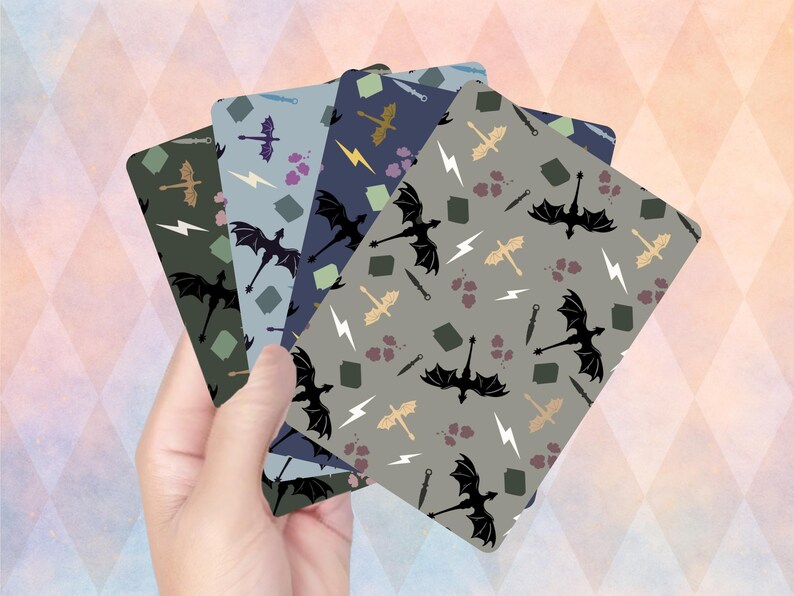 Op de afbeelding: Een hand die een stapel kaarten met patronen vasthoudt. Elke kaart heeft een ander kleurenschema met herhaalde illustraties van draken, bliksemschichten en zwaarden. De kleurenschema's omvatten tinten groen, blauw en grijs.