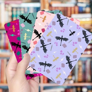 May include: A hand holds a fan of colorful cards with dragon and fantasy-themed patterns. The cards feature dragons, swords, lightning bolts, and other fantasy elements in shades of purple, pink, green, and teal.