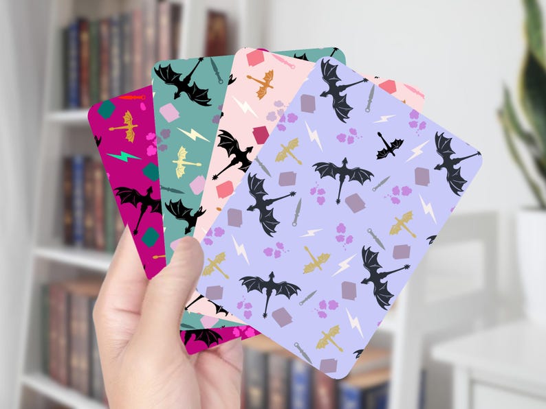 May include: A hand holds a stack of colorful cards with dragon and fantasy-themed patterns. Each card features a different background color: magenta, teal, pink, and lavender. The patterns include black dragons, swords, lightning bolts, and other fantasy elements.