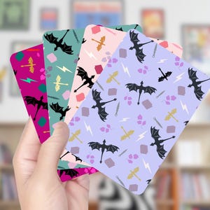 May include: A hand holds a fan of colorful cards with dragon and fantasy-themed patterns. Each card features a different background color: fuchsia, teal, pink, and lavender. The patterns include black dragons, swords, lightning bolts, and other fantasy elements.