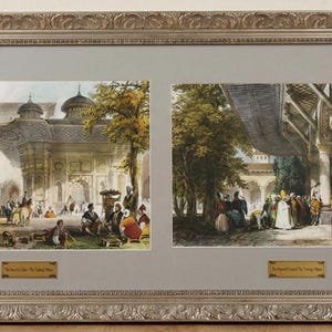 May include: A framed print featuring two detailed, colorful illustrations of an architectural scene with people. The frame is silver-toned with ornate detailing. The prints have gold-toned labels with text.