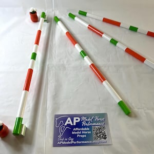 May include: Model horse jump poles in red, white, and green. The poles are striped and appear to be made of wood. The image also includes a small business card with the text "AP Model Horse Performance" and a QR code.