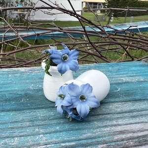 May include: A set of three ceramic mugs with a speckled, matte finish. Each mug features a different color: light blue, cream, and gray. The mugs have a simple, modern design with a rounded shape and a comfortable handle.