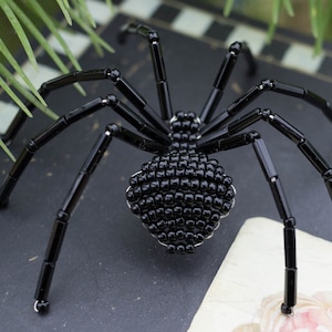 May include: A black beaded spider with eight legs. The spider is made of small black beads and has a shiny finish.
