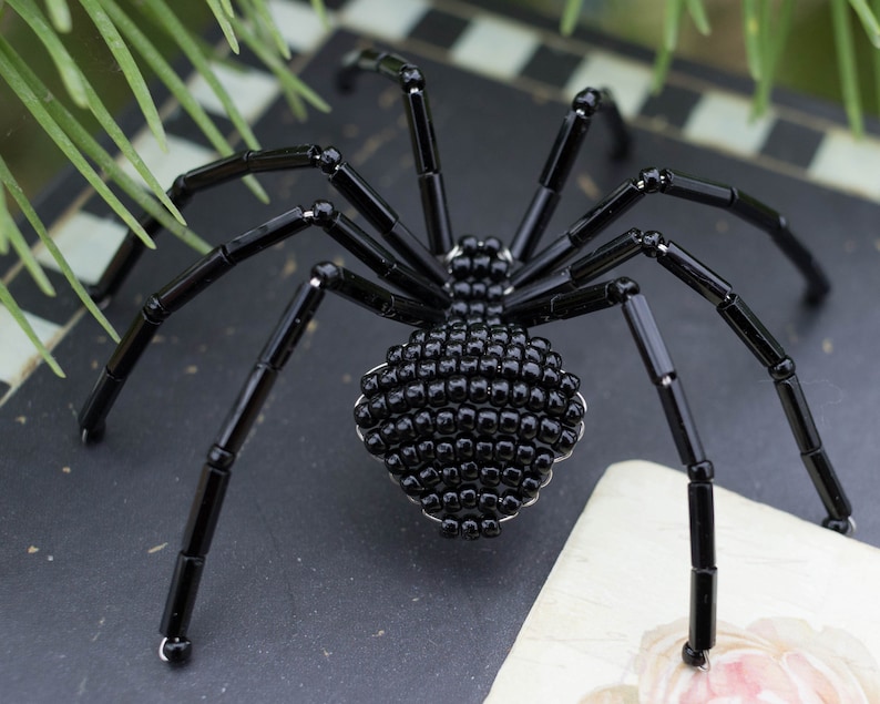 May include: A black beaded spider with eight legs. The spider is made of small black beads and has a shiny finish.