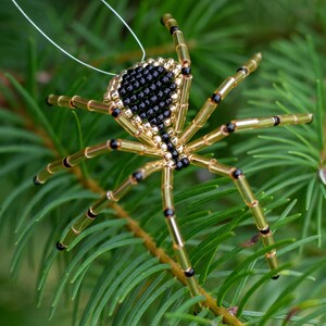 May include: A gold and black beaded spider ornament hanging from a white string. The spider has a black body and gold legs with black accents.