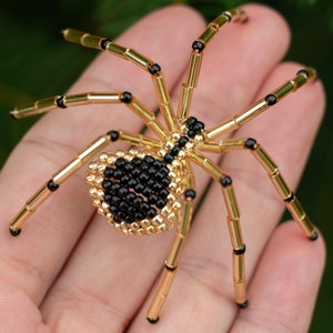 May include: A black and gold beaded spider with eight legs. The spider is made of small beads and is about the size of a hand.