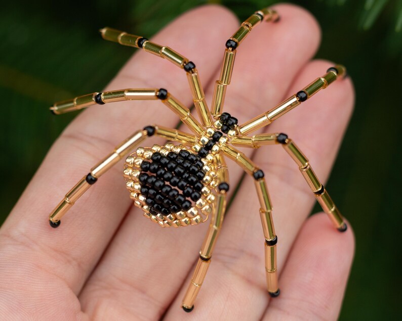 May include: A black and gold beaded spider with eight legs. The spider is made of small beads and is about the size of a hand.