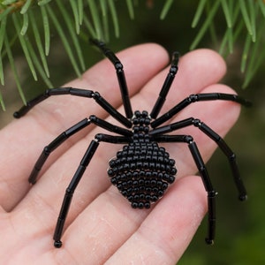 May include: A black beaded spider with eight legs and a round body. The spider is made of small black beads and is about the size of a quarter.