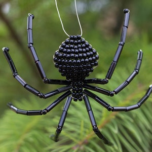 May include: A black beaded spider ornament with eight legs and a round body. The spider is hanging from a silver string.