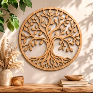 May include: A circular wooden wall art piece featuring a laser-cut design of a tree with intricate branches, leaves, and exposed roots enclosed within a solid wooden frame. The natural light brown wood grain is visible throughout the entire structure.