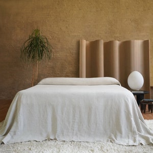 May include: A white linen bedspread with a headboard made of wood panels. The headboard has a wavy design and is against a brown wall.