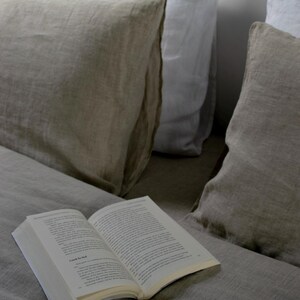 May include: A book titled "Back to Bed" is lying open on a bed with two linen pillows. One pillow is white and the other is beige.
