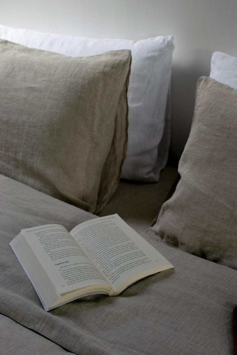 May include: A book titled "Back to Bed" is lying open on a bed with two linen pillows. One pillow is white and the other is beige.