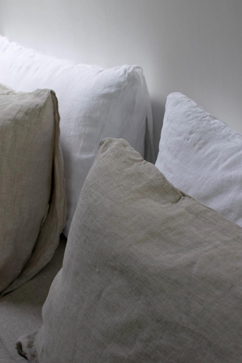 May include: Three pillows, one beige, one white, and one off-white, arranged on a bed. The pillows are made of linen and have a relaxed, casual look.