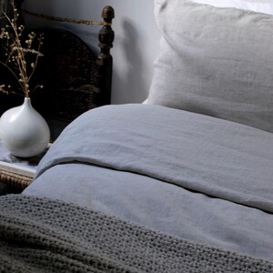 May include: A gray linen duvet cover with a gray knitted throw blanket on top. The duvet cover is on a bed with a white and gray linen pillow.