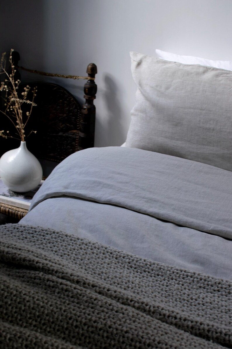 May include: A gray linen duvet cover with a gray knitted throw blanket on top. The duvet cover is on a bed with a white and gray linen pillow.