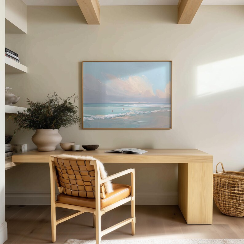 May include: A light wood desk with a framed beach scene painting, a woven leather chair, and a large beige vase with greenery. A woven basket sits on the floor. The room has a neutral color palette.