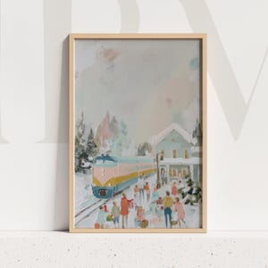 May include: Framed art print of a winter scene with a train arriving at a snow-covered station. The train is blue, pink, and yellow. People are gathered on the platform, and a light blue building with snow-covered roof is in the background.