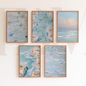 May include: Five framed art prints with beach and ocean scenes. The paintings feature sailboats, swimmers, surfers, and coastal landscapes in shades of blue, white, and tan. Each print is in a light brown wooden frame.
