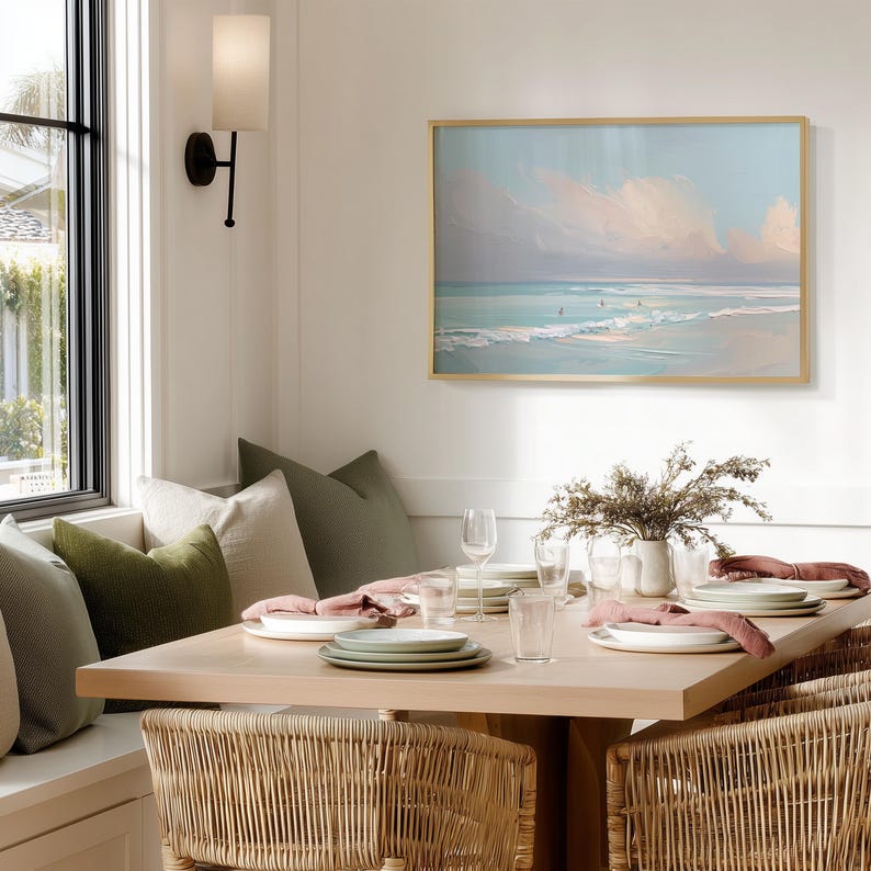 May include: A dining room scene featuring a light wood table set with white plates, green plates, and pink napkins. Wicker chairs surround the table. A framed beach landscape painting hangs on the wall.