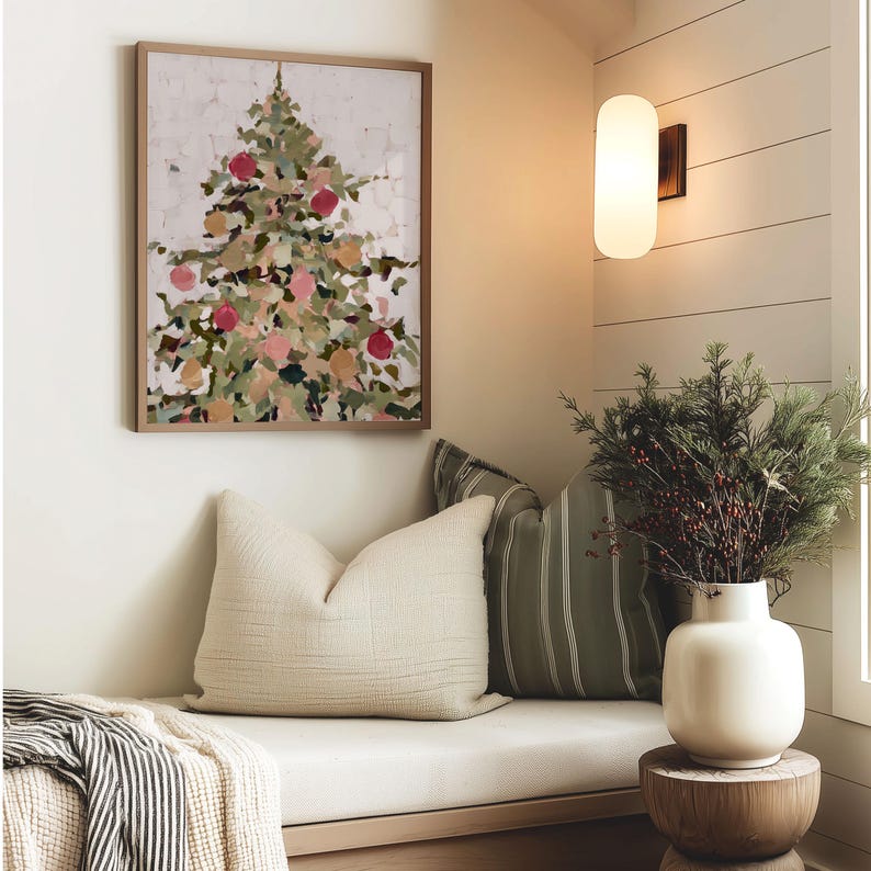 May include: A framed abstract painting of a Christmas tree with red and pink ornaments hangs above a bench with pillows. A white vase with greenery sits on a wooden side table. A wall sconce provides soft lighting.