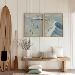 Puede incluir: Interior de tem&aacute;tica costera con una tabla de surf de madera, remos y dos pinturas abstractas enmarcadas del oc&eacute;ano. Un banco de madera sostiene un jarr&oacute;n con ramas secas, almohadas y una alfombra, creando un ambiente sereno y playero.