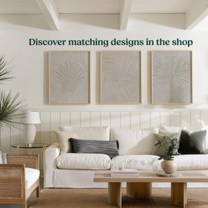 K&ouml;nnte beinhalten: Ein Wohnzimmer mit wei&szlig;em Sofa, Holztisch und drei gerahmten Kunstwerken mit Muschel-, Blatt- und Palmenmotiven. Der Text "Discover matching designs in the shop" ist &uuml;ber den Kunstwerken zu sehen.