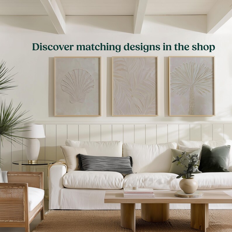 K&ouml;nnte beinhalten: Ein Wohnzimmer mit wei&szlig;em Sofa, Holztisch und drei gerahmten Kunstwerken mit Muschel-, Blatt- und Palmenmotiven. Der Text "Discover matching designs in the shop" ist &uuml;ber den Kunstwerken zu sehen.