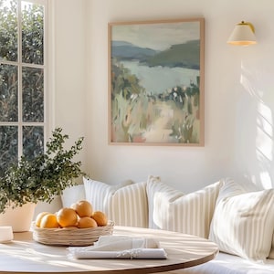 May include: A dining area with a round wooden table, a woven basket of oranges, and striped pillows. A framed landscape painting hangs on the wall. A window with natural light and a potted plant are also visible.