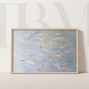 May include: A framed art print featuring an abstract painting of surfers in the ocean. The artwork depicts numerous surfers on surfboards in a light blue sea with white clouds. The frame is a light wood color.