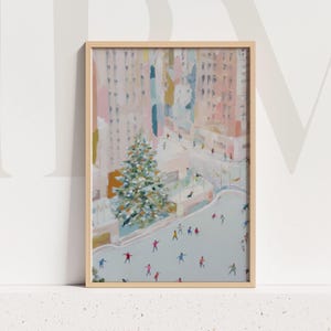 May include: A framed art print depicts an outdoor ice skating scene with a large Christmas tree. The artwork features a light color palette with pink, blue, and white hues. People are skating on the ice, and buildings are in the background.