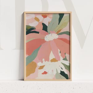 May include: A framed floral art print featuring a large, abstract flower in shades of pink, peach, and white. Green and yellow-brown leaves surround the flower. The artwork is set in a light wood frame.