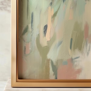 May include: Abstract art print in a gold frame. The artwork features brushstrokes in shades of green, peach, and blue. The painting has a textured appearance, with visible brush marks. The frame is a simple, modern design.