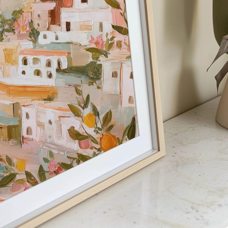 K&ouml;nnte beinhalten: Gerahmter Kunstdruck mit einem abstrakten Gem&auml;lde eines K&uuml;stendorfes. Das Kunstwerk zeigt wei&szlig;e Geb&auml;ude mit orangefarbenen und braunen D&auml;chern, akzentuiert durch rosa Bl&uuml;ten und Zitrusfr&uuml;chte. Der Druck ist in einem hellen Holzrahmen mit wei&szlig;em Passepartout gefasst.