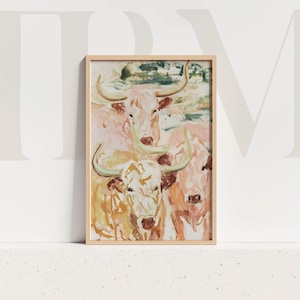 May include: A framed art print depicting a watercolour painting of four longhorn cattle. The artwork uses soft pinks, yellows, and greens, with the cattle's horns prominent. The frame is a light wood colour.