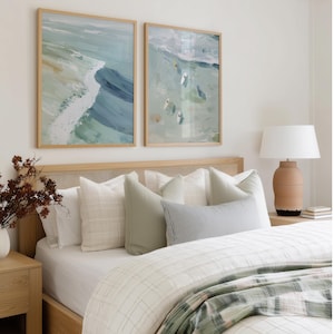 Puede incluir: Decoraci&oacute;n de dormitorio con dos pinturas abstractas enmarcadas de olas en tonos azules y verdes. La cama tiene un cabecero de madera clara, almohadas blancas y un edred&oacute;n a cuadros. Una l&aacute;mpara con base de terracota est&aacute; sobre la mesita de noche.