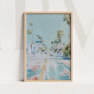 May include: An oil painting in a light wood frame depicts a street lined with palm trees under a light blue sky. The road has yellow lines, and the buildings are white. The artwork has a textured, impressionistic style.
