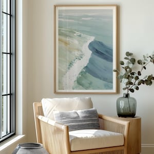 Puede incluir: Impresi&oacute;n art&iacute;stica abstracta de olas oce&aacute;nicas en tonos azules, verdes y blancos, enmarcada en madera clara. La obra de arte cuelga sobre un sill&oacute;n tejido con un coj&iacute;n blanco y una almohada a rayas. Un jarr&oacute;n con vegetaci&oacute;n se encuentra sobre una mesa auxiliar de madera.