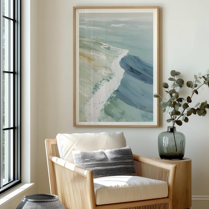 Puede incluir: Impresi&oacute;n art&iacute;stica abstracta de olas oce&aacute;nicas en tonos azules, verdes y blancos, enmarcada en madera clara. La obra de arte cuelga sobre un sill&oacute;n tejido con un coj&iacute;n blanco y una almohada a rayas. Un jarr&oacute;n con vegetaci&oacute;n se encuentra sobre una mesa auxiliar de madera.