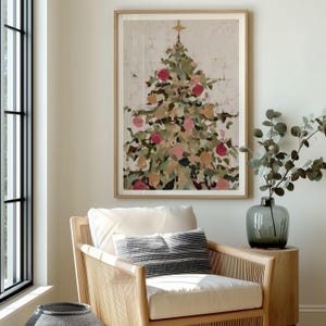May include: A framed print of a Christmas tree with a gold star on top. The tree is decorated with red and gold ornaments. The print is in a light wood frame and hangs above a wicker chair with a white cushion and a striped pillow.