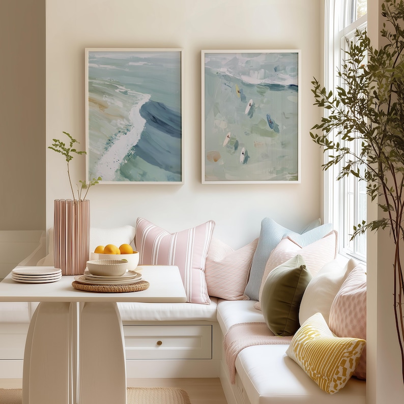 Puede incluir: Una escena interior acogedora con dos pinturas abstractas del oc&eacute;ano enmarcadas en tonos azules y verdes. Una mesa blanca est&aacute; puesta con platos y un cuenco de naranjas. Cojines decorativos en rosa, azul y amarillo adornan un banco empotrado.
