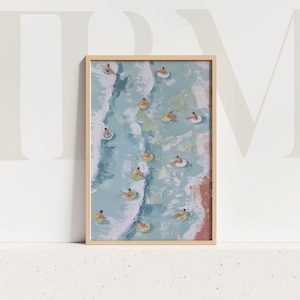 Puede incluir: Una impresión artística enmarcada representa una escena de playa con personas flotando en flotadores en el océano. La obra de arte presenta una paleta de colores azul claro y blanco, con una zona de playa arenosa en la esquina inferior derecha. El marco es de color madera clara.