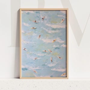 May include: A framed art print depicting a serene ocean scene with numerous surfers on their boards. The artwork features a light blue and white color palette, with a wooden frame. The painting style is impressionistic.
