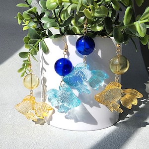 May include: Three pairs of dangle earrings featuring gold-tone chains, clear glass beads, and colorful fish charms. The fish charms are blue, light blue, and yellow.