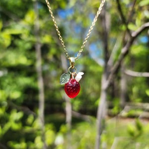Op de afbeelding: Een gouden ketting met een rode glazen aardbeienhanger. De aardbei heeft een groen blaadje en een witte parel accent.