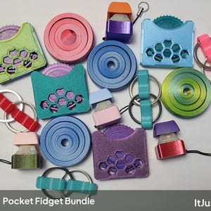 Puede incluir: Una colección de juguetes fidget impresos en 3D que incluye discos circulares, estuches con patrón de panal y engranajes internos, interruptores mecánicos con cordones y anillos unidos en colores como rosa, azul, verde y morado.