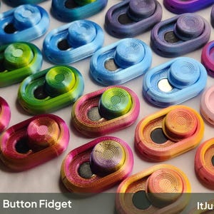 Może przedstawiać: Kolekcja owalnych zabawek typu fidget z przyciskiem w różnych kolorach, w tym gradientach niebieskiego, zielonego, różowego, fioletowego i pomarańczowego. Każda zabawka ma okrągły przycisk i ciemny środek. Widoczny jest tekst Button Fidget oraz ItJustClicks3D.