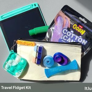 May include: A travel fidget kit containing a teal digital writing tablet with a stylus, a Zuru Oosh Cotton Candy scented putty pouch, a square teal and white pop-it, a green tube, a blue mesh marble toy, a blue circular toy, and a blue block.